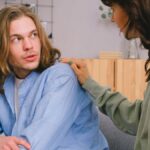 Concentrated woman talking and touching shoulder of pensive male in light room in daytime