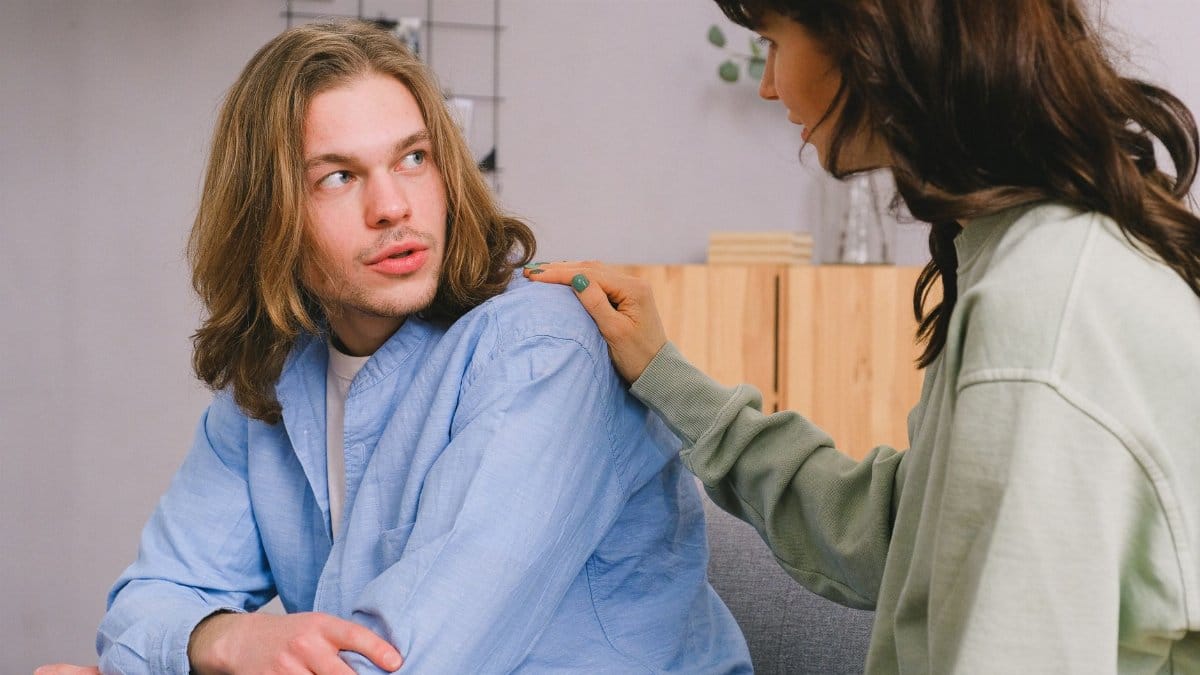 Concentrated woman talking and touching shoulder of pensive male in light room in daytime