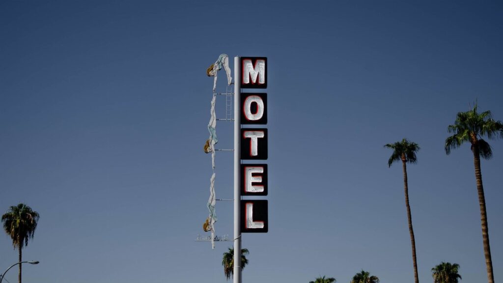 Low angle of motel signboard on metal pillar located at roadside near tall palms against cloudless blue sky