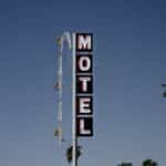 Low angle of motel signboard on metal pillar located at roadside near tall palms against cloudless blue sky