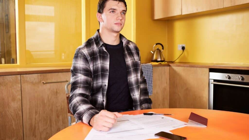 Adult man sitting at kitchen table reviewing documents with focus and concentration.
