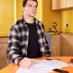 Adult man sitting at kitchen table reviewing documents with focus and concentration.