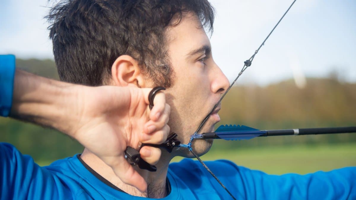 Close-up of a man aiming a bow and arrow outdoors, perfecting his archery skills.