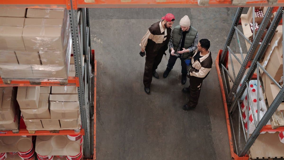 Three warehouse workers discussing logistics in an industrial storage area.