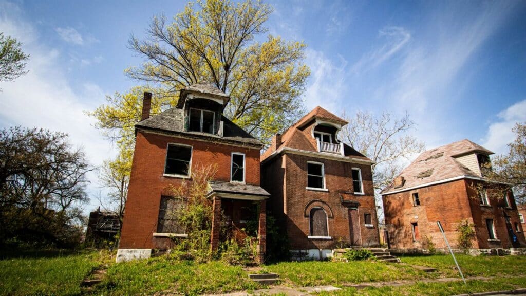 Three abandoned brick houses in a suburban neighborhood under a clear blue sky.