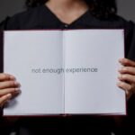 A graduate in cap and gown displays a diploma reading 'not enough experience', highlighting job market challenges.