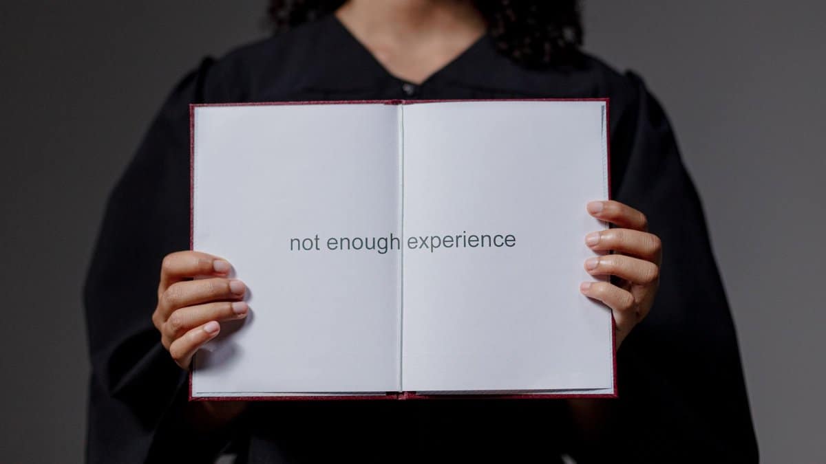 A graduate in cap and gown displays a diploma reading 'not enough experience', highlighting job market challenges.