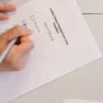 Hand placing vote on ballot form during election process, highlighting civic duty and democracy.