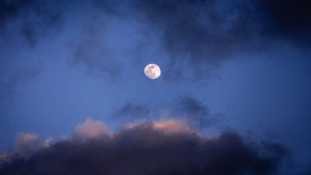 Captivating full moon with dynamic clouds in the twilight sky creating a dramatic scene.