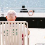 A senior man sits by the sea in Lisbon, enjoying a peaceful sunny day. Perfect for travel and summer themes.