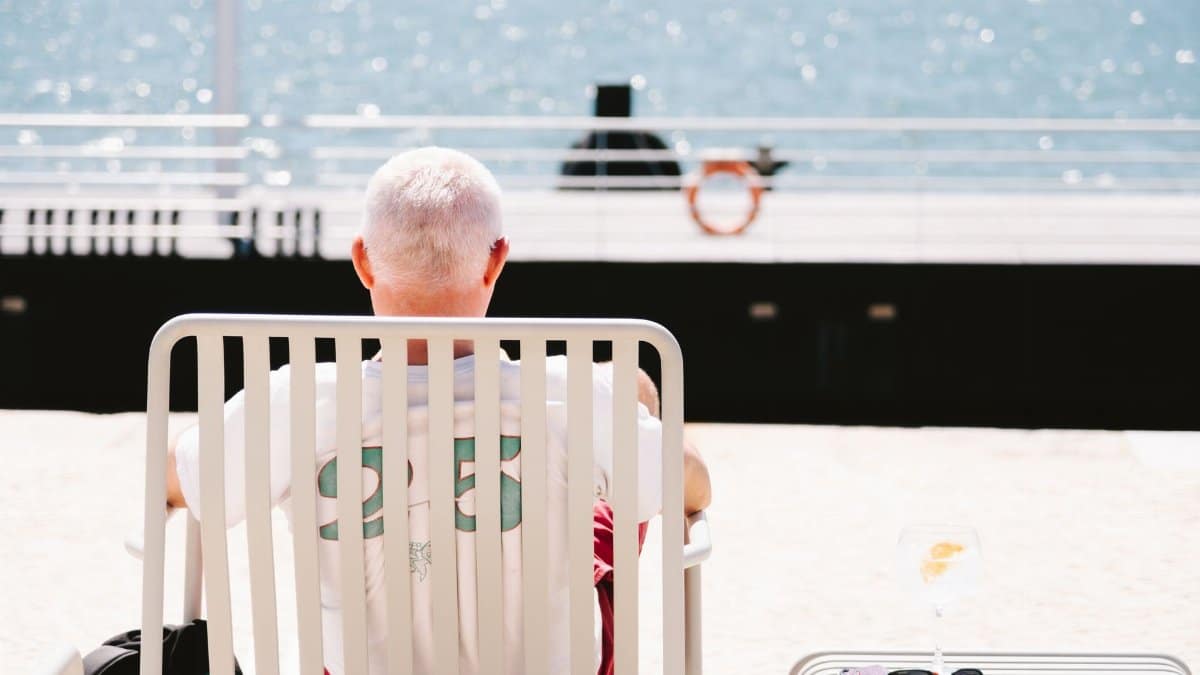 A senior man sits by the sea in Lisbon, enjoying a peaceful sunny day. Perfect for travel and summer themes.