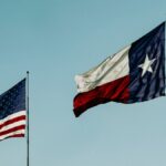 American and Texas flags waving under a clear blue sky, symbolizing patriotism and freedom.