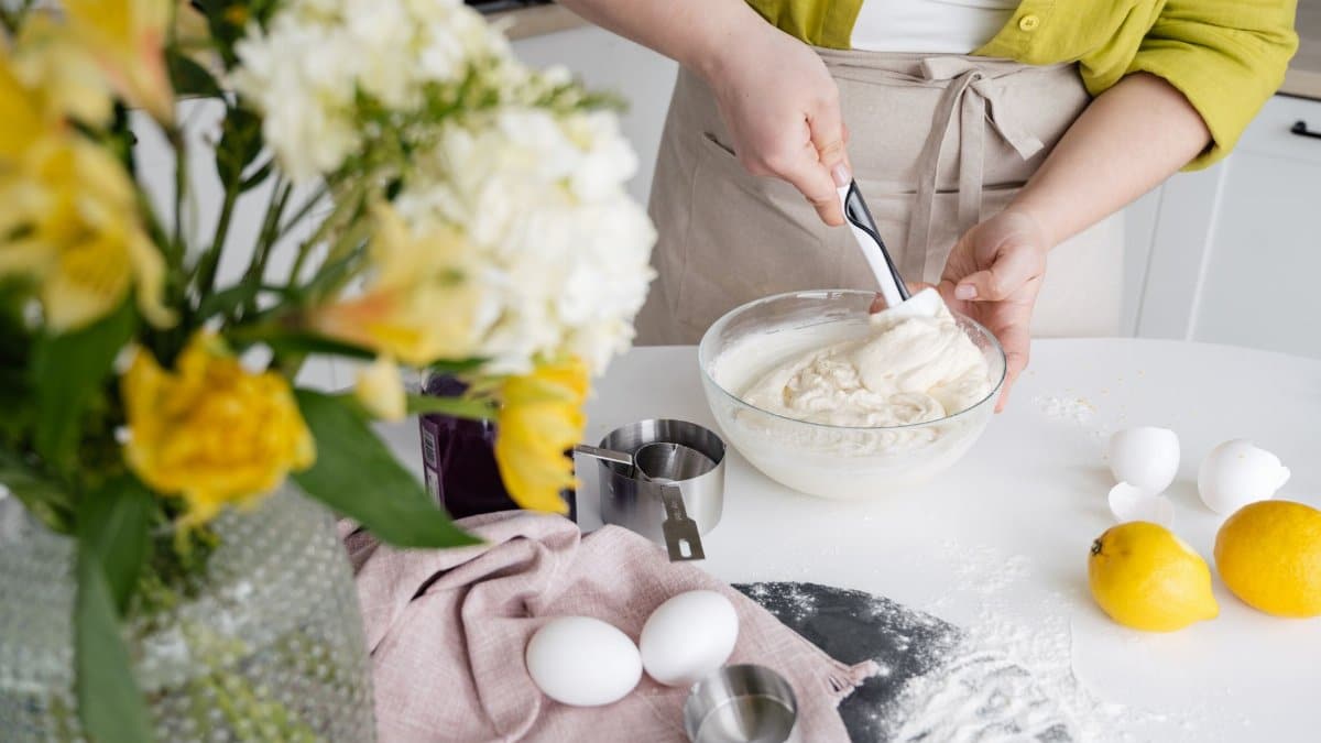 Woman mixing cake batter in a modern kitchen with fresh lemons and flour surrounding.