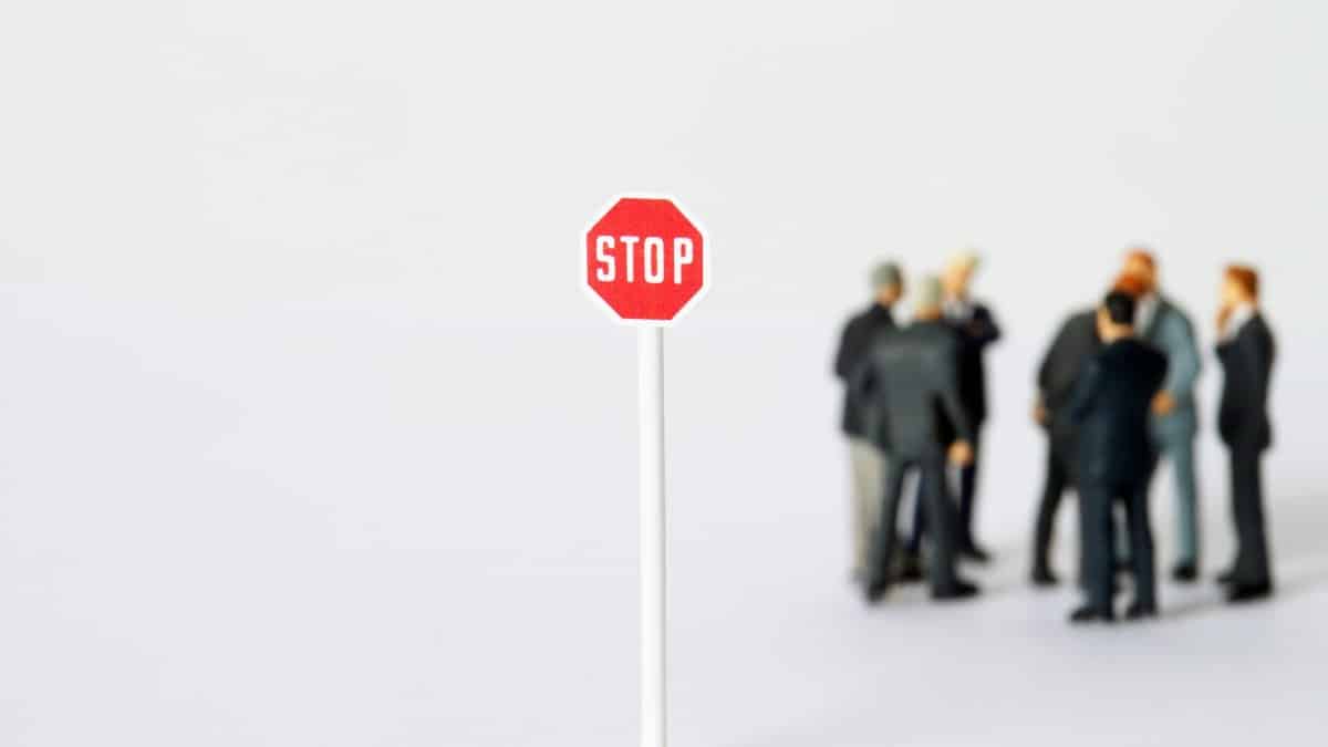 A miniature stop sign stands out with blurred figures in business attire, representing a conceptual business metaphor.