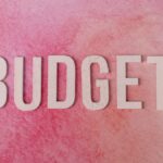 The word 'BUDGET' on a pink textured background emphasizes financial planning.