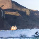 A surfer rides a wave near the iconic Golden Gate Bridge in San Francisco, California.
