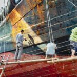 Three workers refurbishing a ship's hull in Shantou City, Guangdong Province, China.