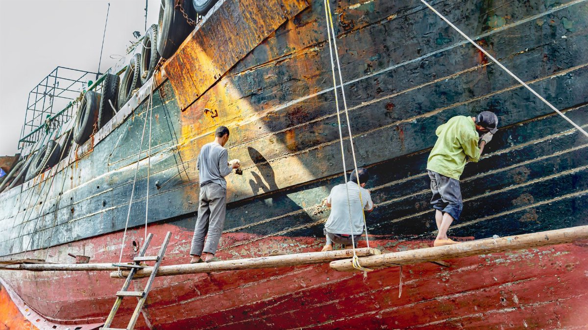 Three workers refurbishing a ship's hull in Shantou City, Guangdong Province, China.