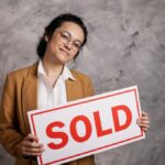 Confident real estate agent holding a 'Sold' sign indoors, symbolizing successful property sale.