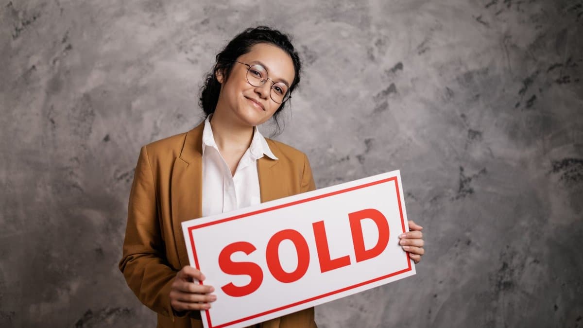 Confident real estate agent holding a 'Sold' sign indoors, symbolizing successful property sale.