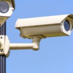 Outdoor security cameras mounted on a pole against a clear blue sky, ensuring vigilant surveillance.