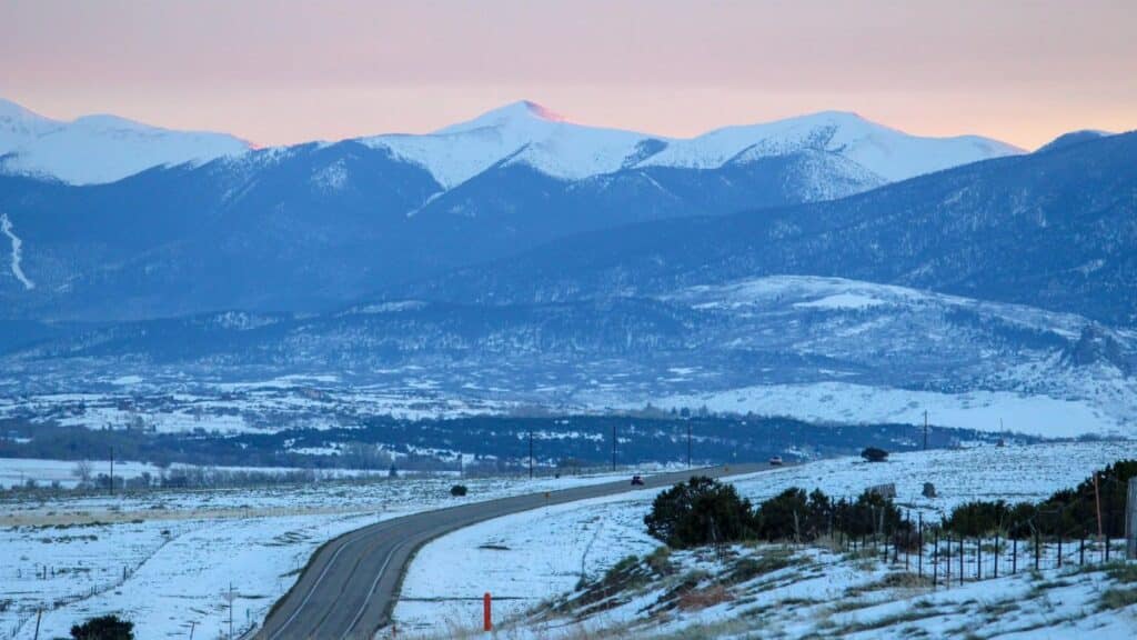 Snow-covered road winding through the winter landscape of Crested Butte, Colorado with mountain views at sunset.