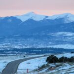 Snow-covered road winding through the winter landscape of Crested Butte, Colorado with mountain views at sunset.