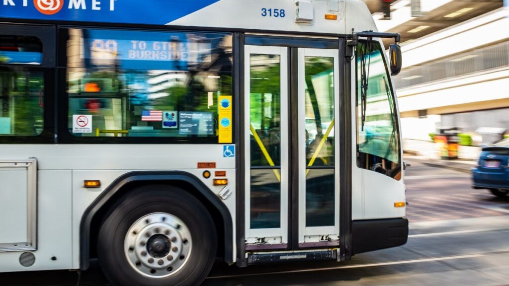A city bus from TriMet transit system speeds through an urban street during the day.