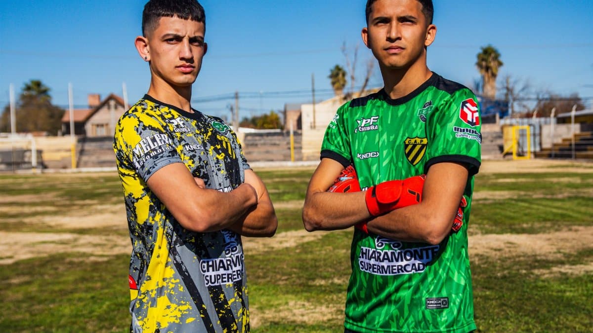 Two young men proudly posing on a soccer field, wearing team jerseys.