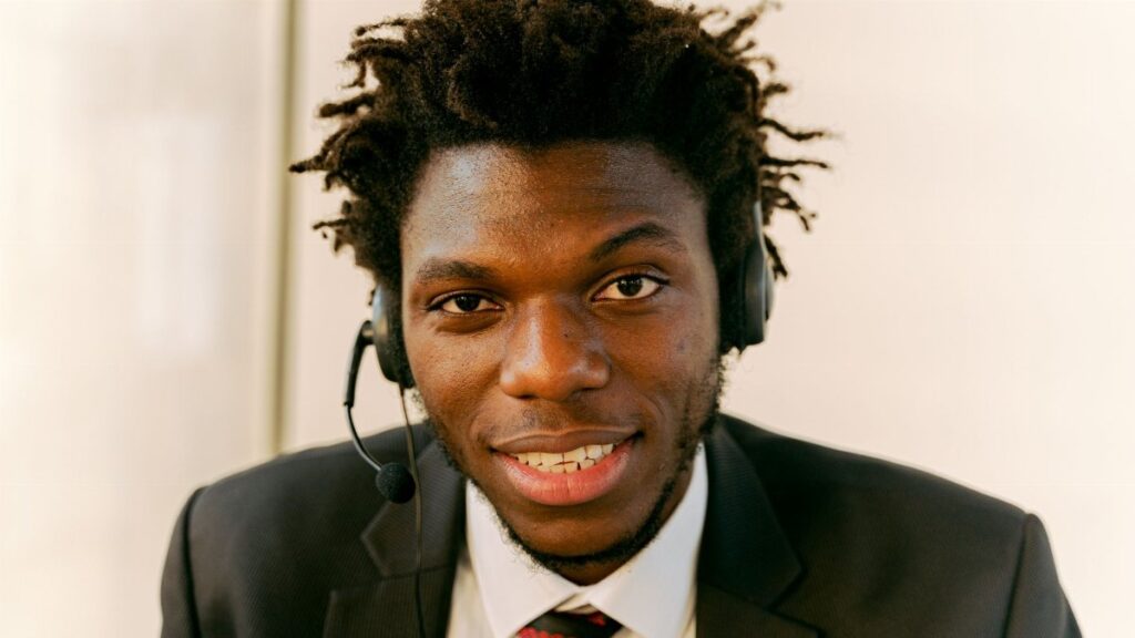 Professional call center agent wearing a suit and headset, smiling at the camera.