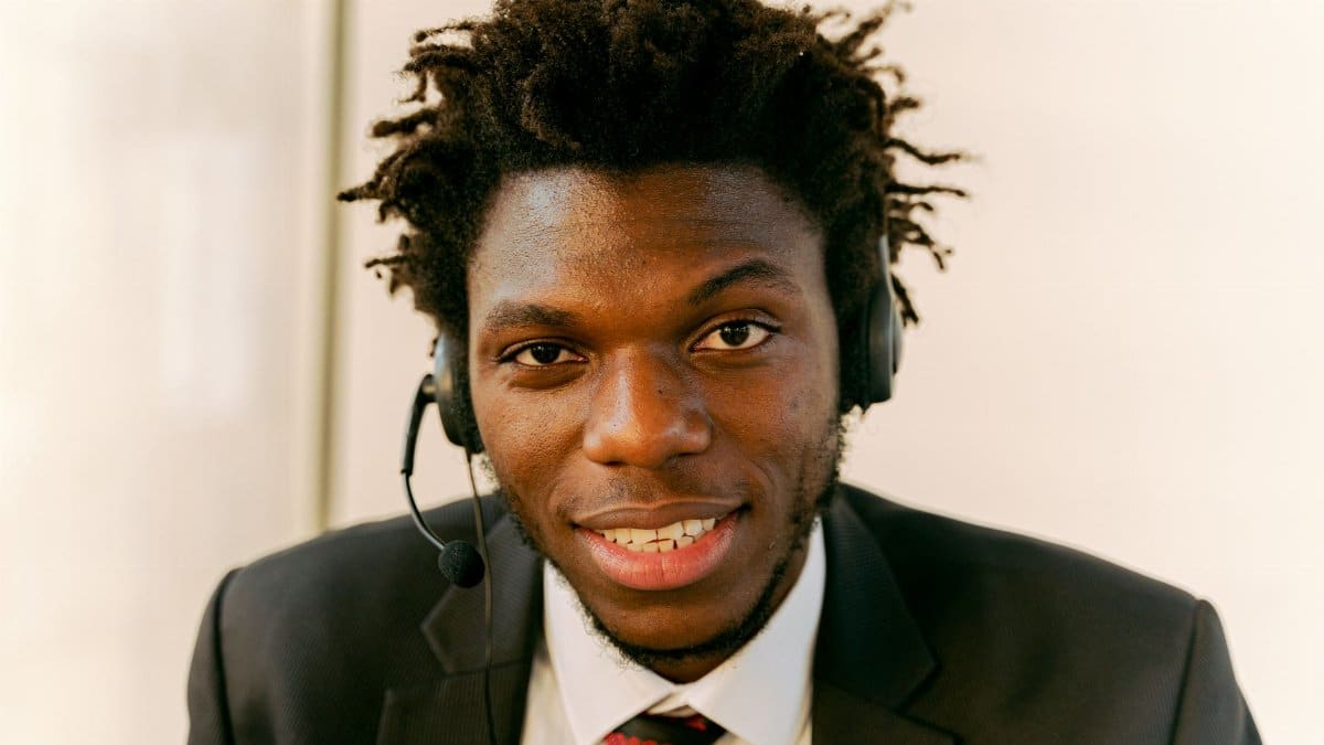 Professional call center agent wearing a suit and headset, smiling at the camera.