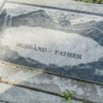 Close-up of a weathered granite tombstone with engraving of 'Husband' and 'Father' including dates 1919-1998.