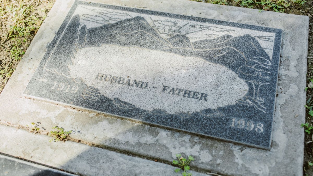 Close-up of a weathered granite tombstone with engraving of 'Husband' and 'Father' including dates 1919-1998.
