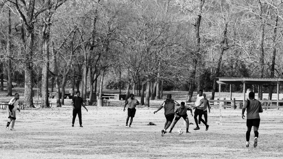 A group of men playing soccer in a park in Arlington, Texas, captured in black and white.