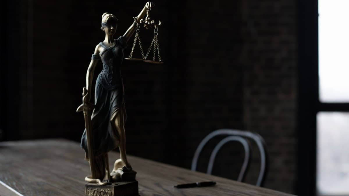 Lady Justice figurine on wooden table in dimly lit room symbolizes law and fairness.
