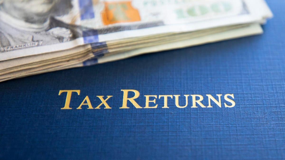 Close-up of tax returns folder beside a stack of American dollars, representing finance and accounting.