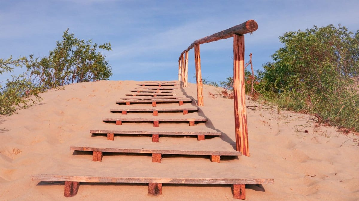 Wooden stairs leading over a sandy dune with clear blue skies, perfect for a peaceful beach walk.