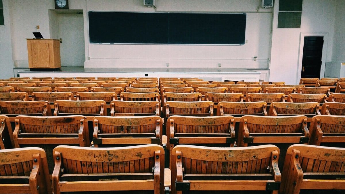 An empty lecture hall featuring wooden chairs and a large blackboard.