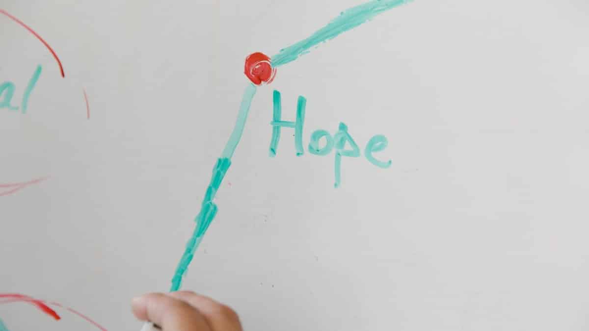 Close-up of a hand drawing on a whiteboard, illustrating hope with colorful markers.