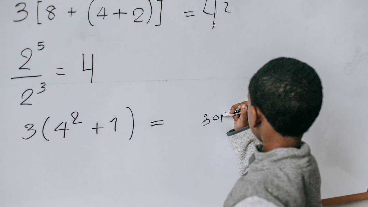 Back view of anonymous African American boy writing on whiteboard while doing sums on mathematics class