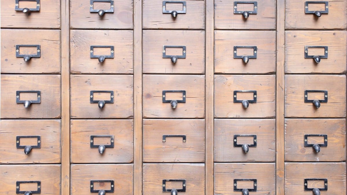 Background of wall full of many similar aged shabby vintage wooden drawers with metal round handles
