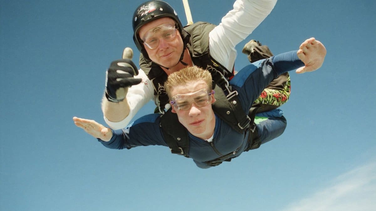 Two men tandem skydiving, experiencing the thrill of free fall against a clear blue sky.
