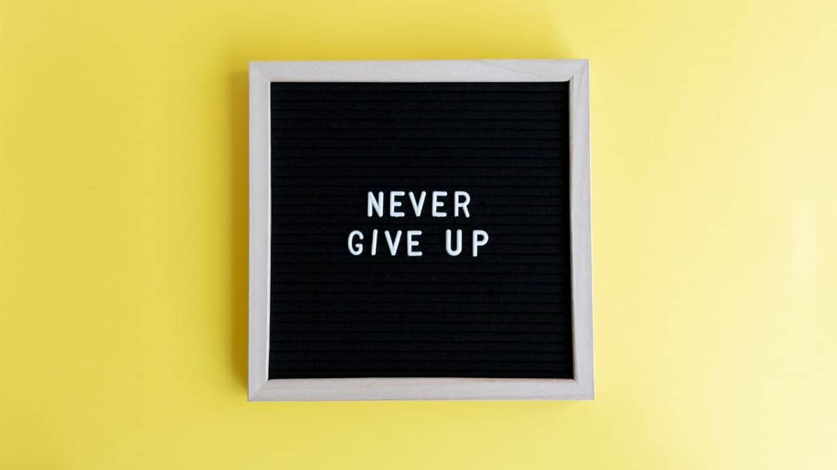 Black felt board with 'Never Give Up' on a bright yellow background for motivation.