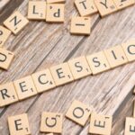 Wooden letter tiles on a wooden surface spell out the word "Recession," symbolizing economic downturn.