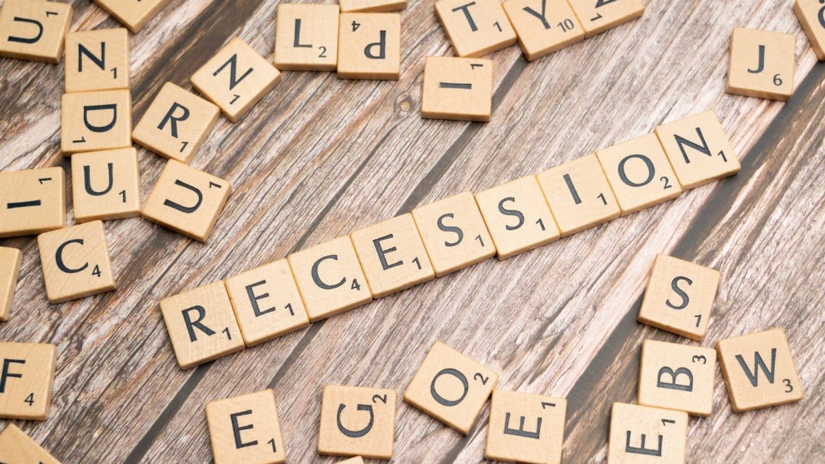 Wooden letter tiles on a wooden surface spell out the word "Recession," symbolizing economic downturn.