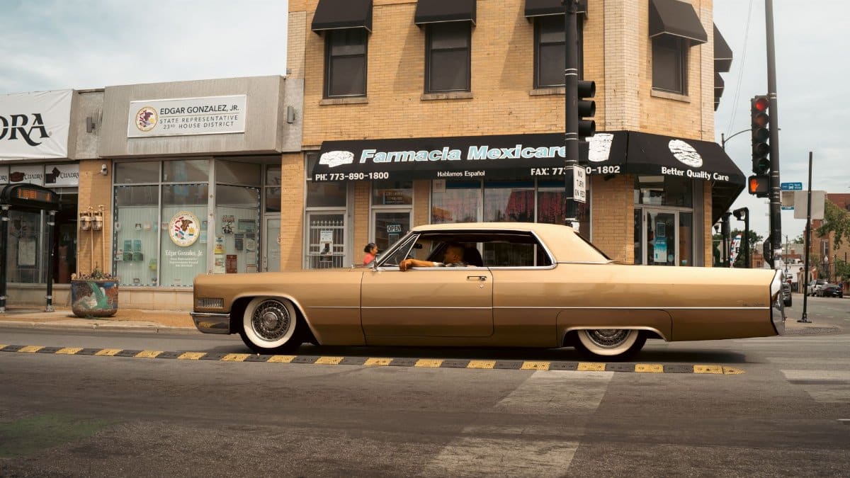 Classic car driving past Mexican pharmacy in Chicago, capturing urban street atmosphere.
