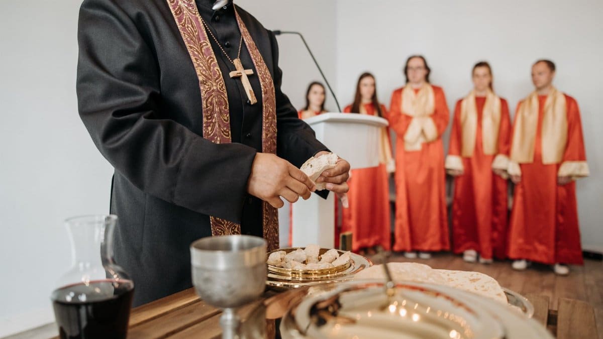 A pastor conducts communion during a church service with a choir in the background.