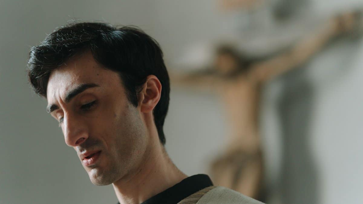 Close-up of a thoughtful clergy member with a blurred crucifix in the background.