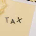 Close-up of a yellow lined paper with metal letters spelling 'tax', surrounded by crumpled paper.