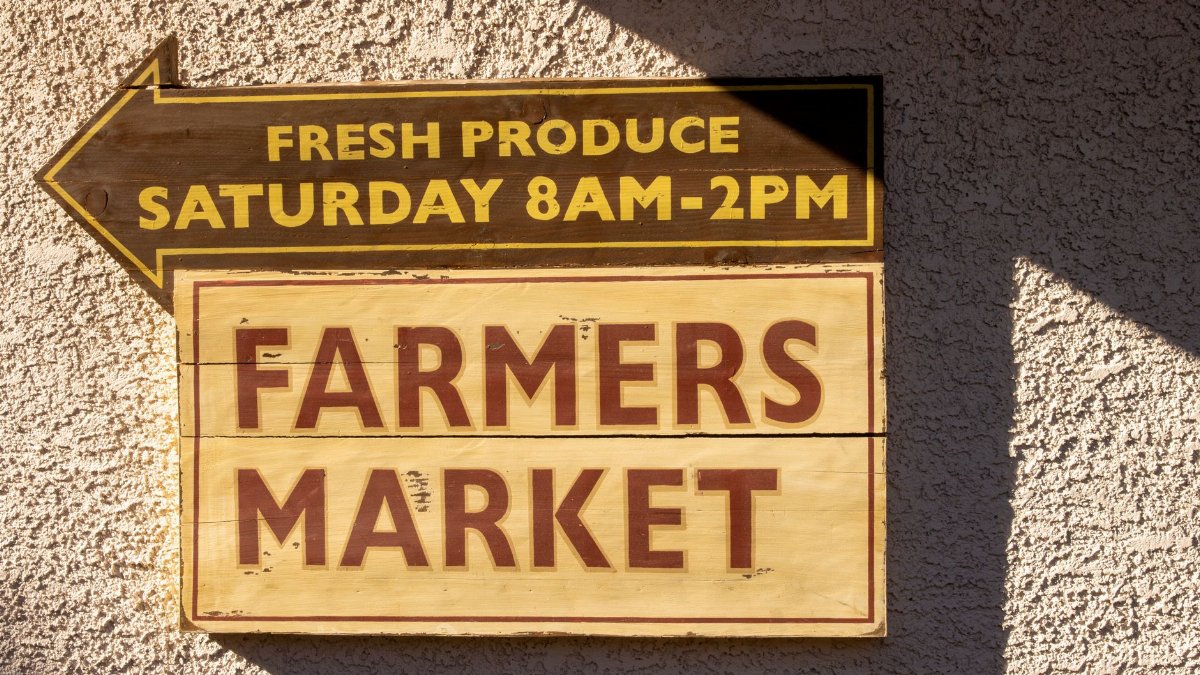 Brightly painted farmers market sign indicating fresh produce times.